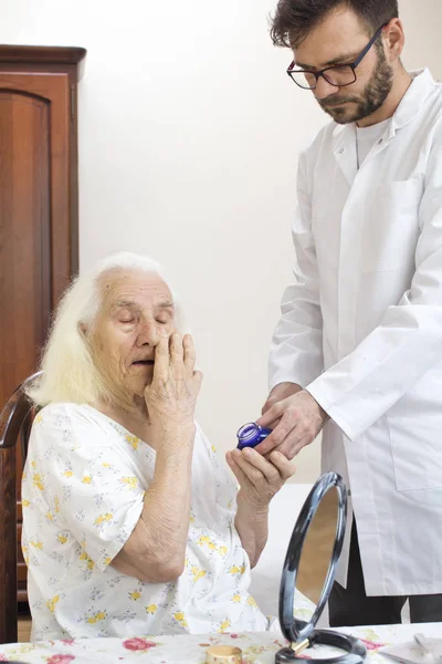 Care of an old woman. The old woman smears her face with cream. Elderly care.