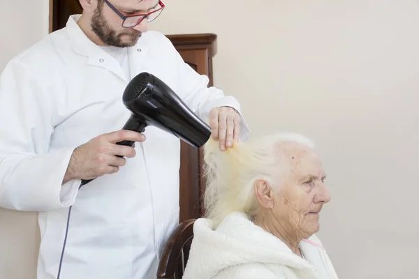 Enfermera Masculina Seca Cabello Una Anciana Sentada Una Silla — Foto de Stock