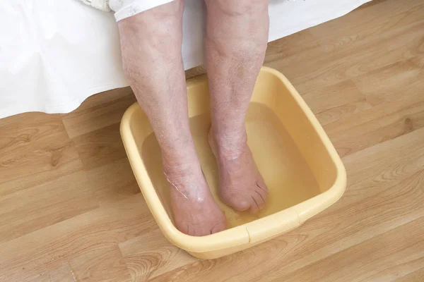 The legs of an old woman soak in a bowl of water.