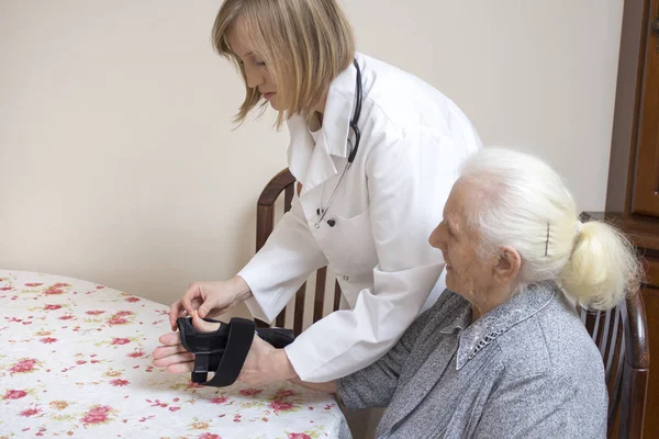 Lääkäri Laittaa Vakaajan Pöydässä Istuvan Vanhan Naisen Käteen — kuvapankkivalokuva