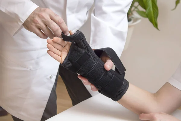 Orthopedic practitioner assumes a black hand stabilizer on a female patient\'s hand.