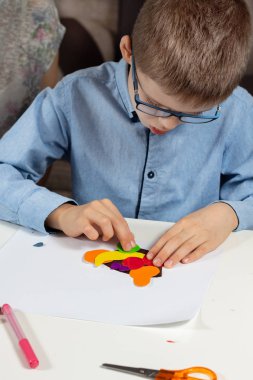 Oğlan mavi tişört ve gözlük oturur bir beyaz Resepsiyon ve tutkal renkli meyve şekillere renkli kağıttan kağıt yönü.