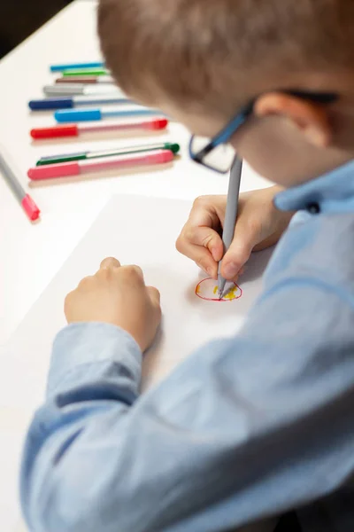 青いシャツとメガネの座っている机で着色されたフェルトのペンと紙のシート上に描画の少年 — ストック写真