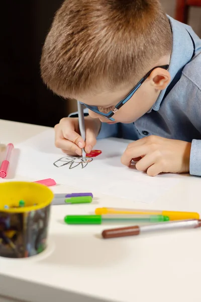 Niño Con Una Camisa Azul Gafas Sienta Escritorio Blanco Dibuja — Foto de Stock