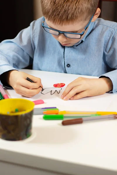 Niño Con Una Camisa Azul Gafas Sienta Escritorio Blanco Dibuja — Foto de Stock