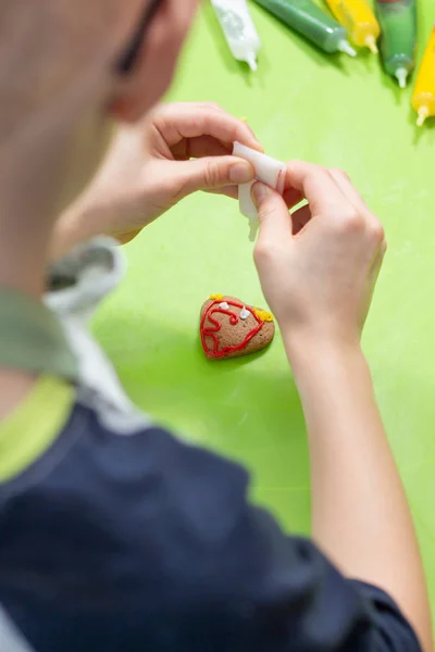 一块心形的饼干躺在一张绿色的咖啡桌上 孩子的手从管子里挤出白色的糖霜 创造装饰 — 图库照片