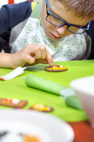 由孩子装饰肉桂饼干 男孩的手形成了一张彩色糖霜的脸 从管子里挤出来 背景中未寻址的饼干 — 图库照片