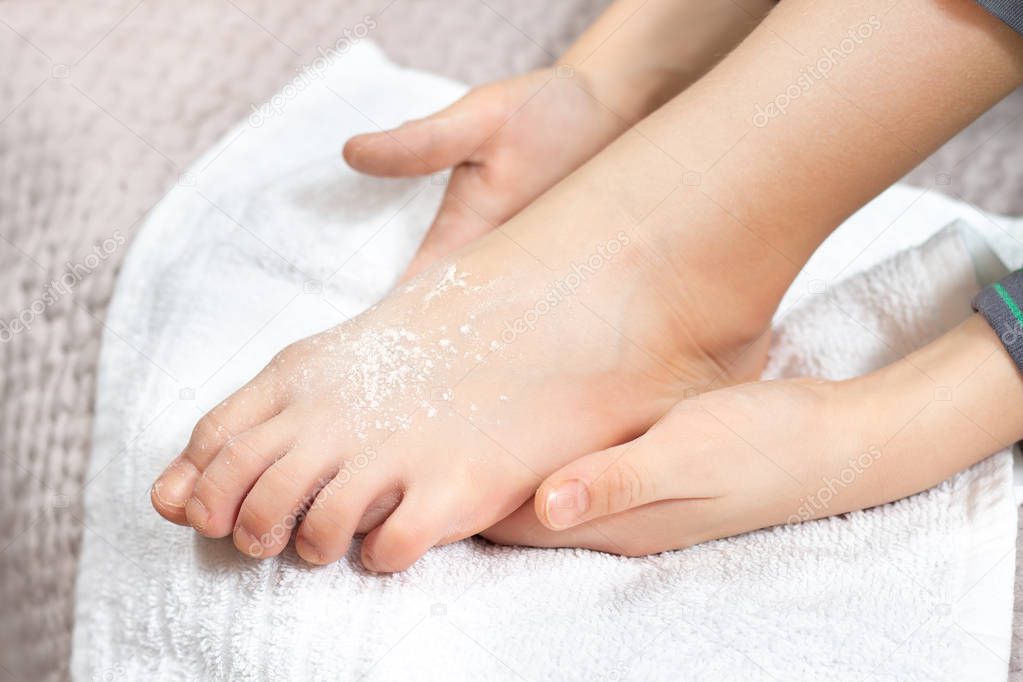 Children's feet sprinkled with a white backfill are lying on a white towel. White powder lies on the skin of the feet.