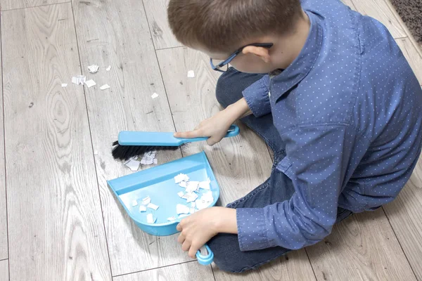 boy\'s hands sweeping the floor. Sweeping the papers with a turquoise duster on a turquoise scoop.