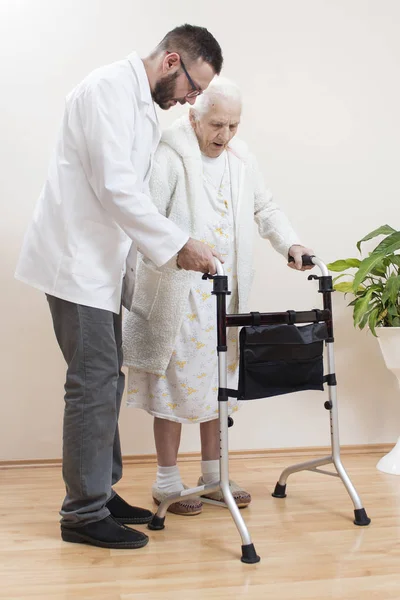 Mężczyzna Pielęgniarka Pomaga Bardzo Starej Kobiety Chodzić Pomocą Walkera Rehabilitacyjnego — Zdjęcie stockowe