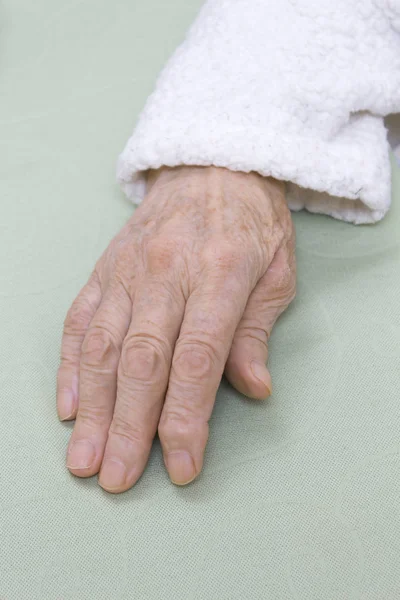 一位穿着白色浴袍的老妇人的手 背景很轻 一位老妇人的手在浅色背景上的白色浴袍的旧损坏皮革 — 图库照片