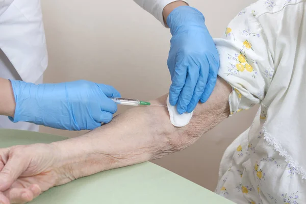 Intravenous injection into the vein of a very old woman. Nurse in disposable gloves gives the medicine intravenously in a syringe in the hand of a very old woman.