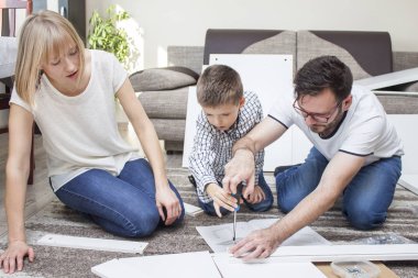 Baba, oğlu ve annesiyle birlikte mobilyaları büküyor. Çocuk bir tornavida tutuyor ve baba vida vida yardımcı olur. Annem bakar ve montaj yönergeleriokur.