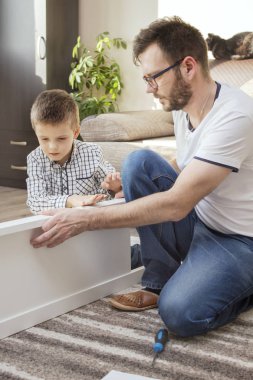 Oturma odasındaki halıda takım çalışması. Adam mobilyaları çeviriyor. Çocuk işte yardımcı olur..