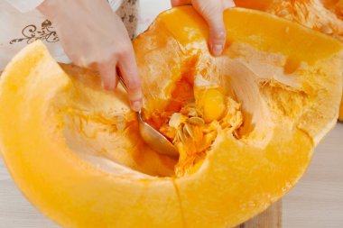 Kadının eli taze kabak püresi ve taşlı bir yemek kaşığı tutuyor. Mutfak tezgahında taze bir balkabağı yatıyor..