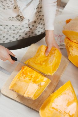 Büyük parçalar halinde balkabağı doğrama tahtasının üzerinde yatıyor. Kadın elleri uzun bir mutfak bıçağını tutar ve balkabağını küçük parçalara ayırır.