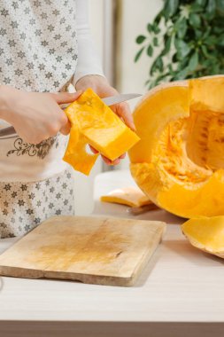 Dişi eller bir parça balkabağı tutuyor ve bir mutfak bıçağıyla derisini yüzüyor. Taze portakal kabağının yarısı mutfak tezgahında yatıyor..