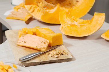 Mutfak bıçağı, balkabağı derisi ve kabak çekirdekleri tahta kesme tahtasının üzerinde yatıyor. Arka planda büyük bir balkabağı ikiye bölünmüş..