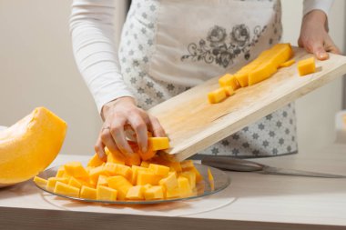 Mutfak önlüklü kadın, doğranmış balkabaklarını tahta kesme tahtasından cam bir tabağa aktarıyor..