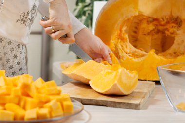 Bal kabağı mutfak tezgahında. Bir kadın mutfak bıçağıyla büyük bir balkabağı kesiyor..