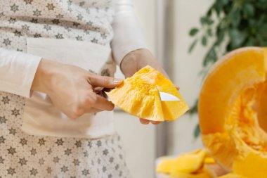 Dişi eller bir parça balkabağı tutuyor ve bir mutfak bıçağıyla derisini yüzüyor. Taze portakal kabağının yarısı mutfak tezgahında yatıyor..