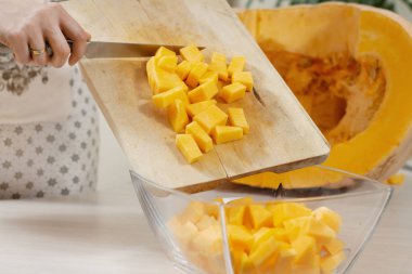 Mutfak önlüklü kadın, doğranmış balkabaklarını tahta kesme tahtasından cam bir tabağa aktarıyor..