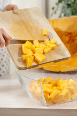 Mutfak önlüklü bir kadın doğrama tahtasından kesilmiş balkabaklarını cam bir tabağa aktarıyor..