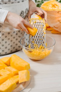 Dişi eller taze bir parça balkabağını tutar ve mutfak rendesine sürterler..