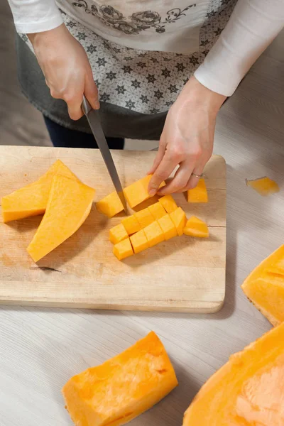 Kadının elleri mutfak bıçağını tutuyor ve mutfak tezgahında duran taze kabağı küçük parçalara ayırıyor..