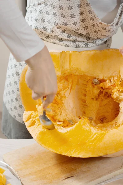 Kadının eli taze kabak püresi ve taşlı bir yemek kaşığı tutuyor. Mutfak tezgahında taze bir balkabağı yatıyor..