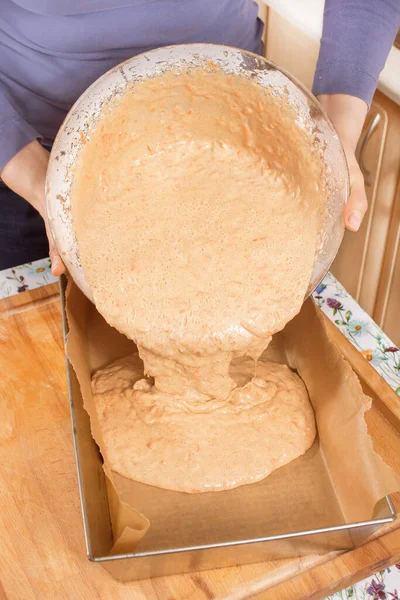 A woman pours the kneaded dough from the bowl into a tin mold lined with baking paper.