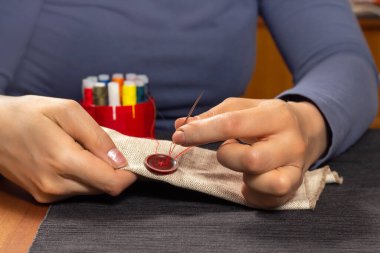 Kadın eli, yırtık bir düğmeyi iğne ve iplikle diker..