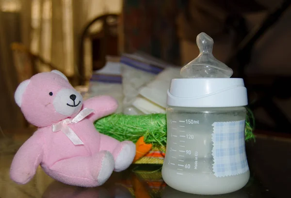 fresh expresed breast milk in baby bottle, pink teddy bear and frozen breast milk in storage bags in background, breastfeeding concept