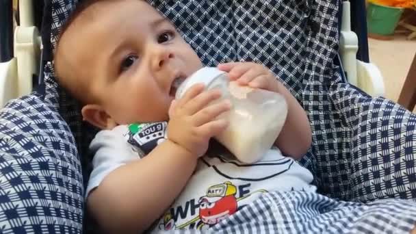 Schattige babyjongen in puschair het drinken van melk uit de fles — Stockvideo