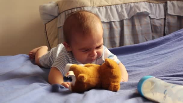 眠そうな生まれたばかりの赤ちゃんの男の子彼のおなかの上でクロール柔らかいおもちゃの子犬とミルク瓶に手を伸ばす — ストック動画
