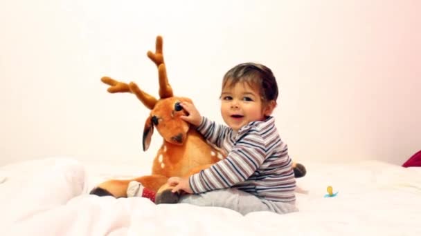 Малыш играет с дорогой игрушкой и снимает носки с застенчивой улыбкой — стоковое видео