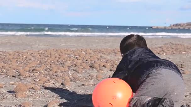 石とカメラを実行しているボールと浜辺で遊んで つと歳半の男の子 — ストック動画