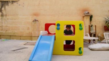 Sevimli iki yaşında çocuk kirli plastik slayt oyun evin arka bahçesinde aşağı kayan ağız çevresindeki çerezleri üzerinden