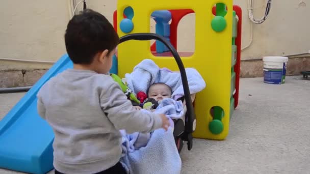 Niedliche Zwei Jahre Alte Junge Schaukelt Seinen Jüngeren Bruder Der — Stockvideo