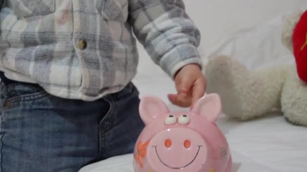 Lindo niño de dos años de edad jugando con alcancía y poner monedas dentro — Vídeos de Stock