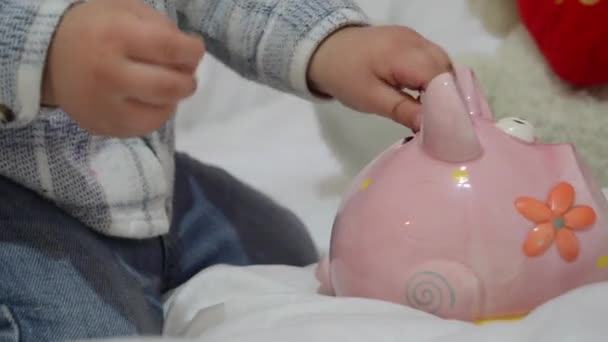 Cute two years old baby boy playing with piggy bank and putting coins inside — Stock Video