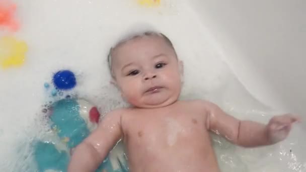 Aranyos 4 hónapos kisfiú feküdt a hab a kád és a gyorsan mozgó — Stock videók