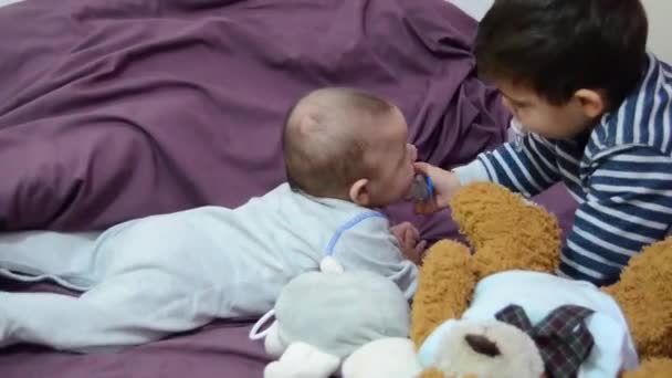 Cute two years old boy giving pacifier to his baby brother — Stock Video