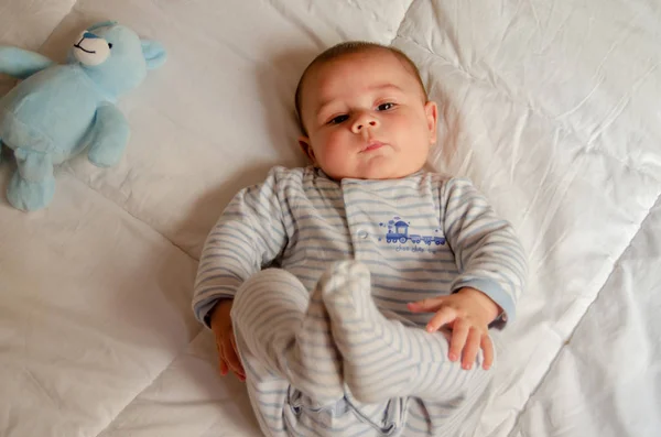 Yatakta yatarken ve bacakları ile oynayan sevimli 4 aylık erkek bebek — Stok fotoğraf