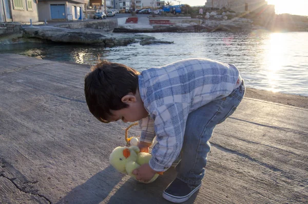 Lindo niño de dos años jugando con pequeño juguete de pollo y cesta con dos huevos de Pascua en el mar doc —  Fotos de Stock