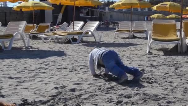 Χαριτωμένο δύο χρονών αγόρι παίζοντας στην αμμώδη παραλία που σέρνεται το φόρεμα — Αρχείο Βίντεο