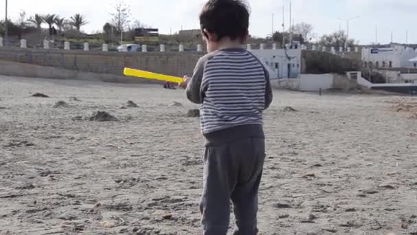 Cute toddler playing with plastic golf stick and sand on the beach with seaweed — Stock Video