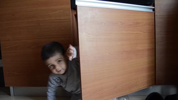 Χαριτωμένο δύο χρονών αγόρι κρύβονται στο ντουλάπι της κουζίνας κάτω από το ενσωματωμένο Owen — Αρχείο Βίντεο