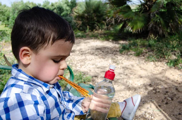 Lindo niño de dos años comiendo bocadillos salados en el parque — Foto de Stock