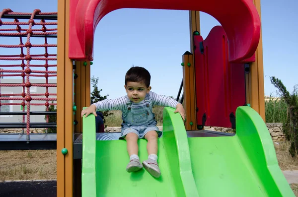 Lindo niño de dos años playig en el parque infantil al aire libre en el tobogán —  Fotos de Stock